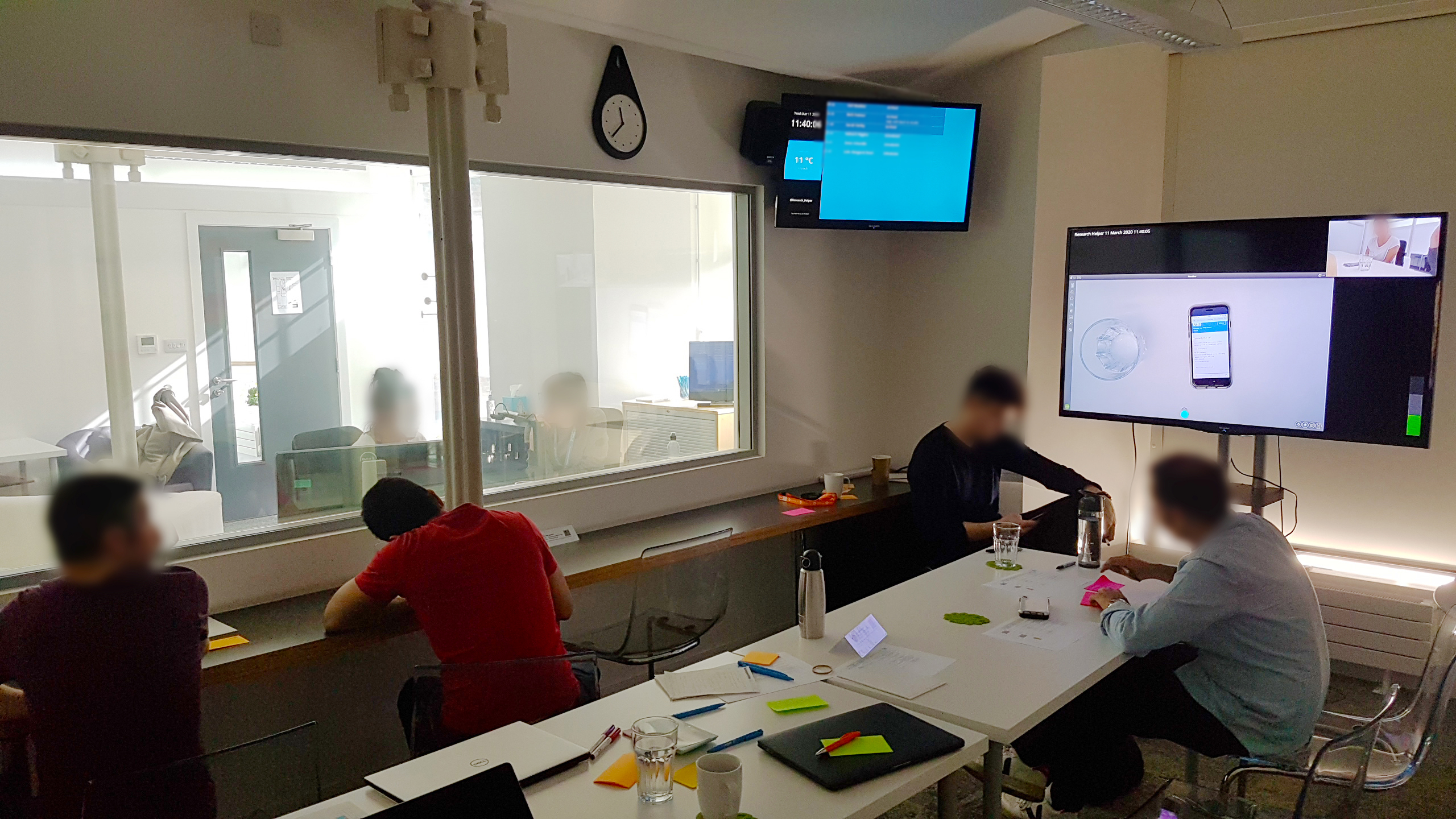 A photo of a user research observation room with people making notes on the session in progress